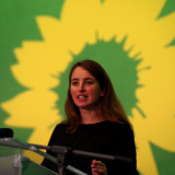 Eine Frau steht an einem Redepult vor einer großen gelben Sonnenblume und blickt entschlossen ins Publikum. Das Bild zeigt Marie Heidenreich beim Landesparteitag im November 2020.