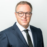 Mario Voigt, Portraitfoto. Er trägt Brille ein blaues Sakko, ein weißes Hemd und eine schwarzer Krawatte.