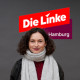 Porträt von Antonia Ivankovic. Eine Frau mit kinnlangen, lockigen, braunen Haaren. Sie trägt einen großen grauen Winterschal um ihren Hals. Hinter ihr ist das Logo der Partei Die Linke zu sehen (weiße Schrift auf rotem Untergrund).