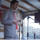 Der Kandidat Emil Pieper steht auf einer Bühne und hält eine Rede im grauen Anzug. Im Hintergrund sind Plakate der PARTEI zu sehen.